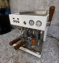تحميل الصورة في عارض المعرض ،A white and stainless steel espresso machine with brown wooden handles, sitting on a gray marble countertop against a patterned wallpaper background.

